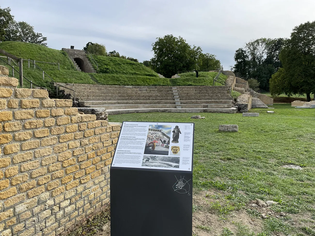 Panneau d'information sur les spectacles antiques; vestiges et gradins du monument à l'arrière-plan
