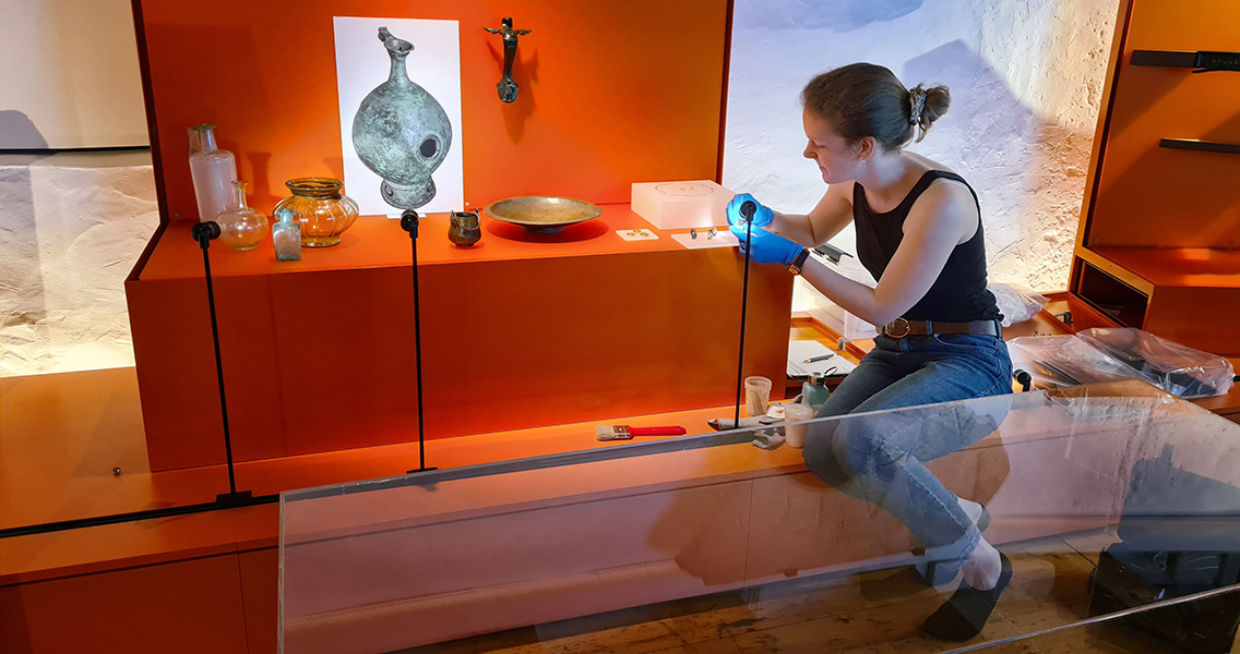 Conservatrice-restauratrice installant et nettoyant des objets dans une vitrine de l'exposition permanente