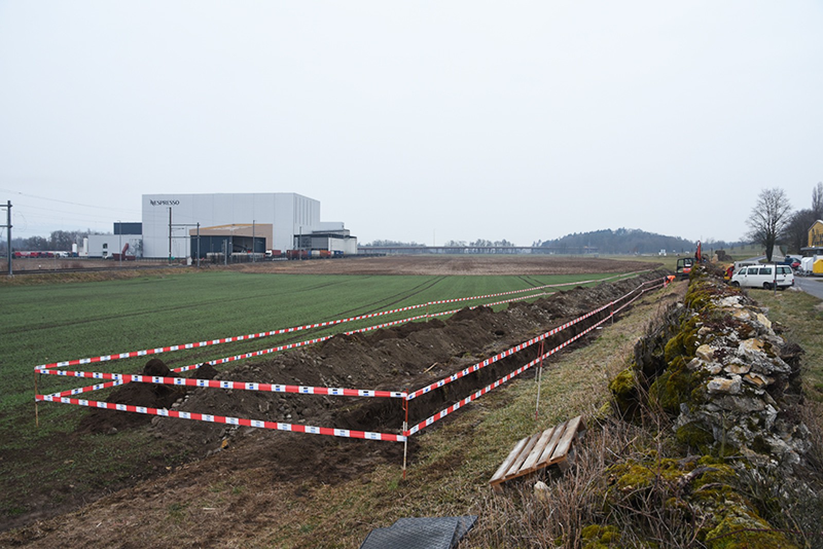 La tranchée creusée pour la pose de conduites électriques et les vestiges du mur d'enceinte (à droite)